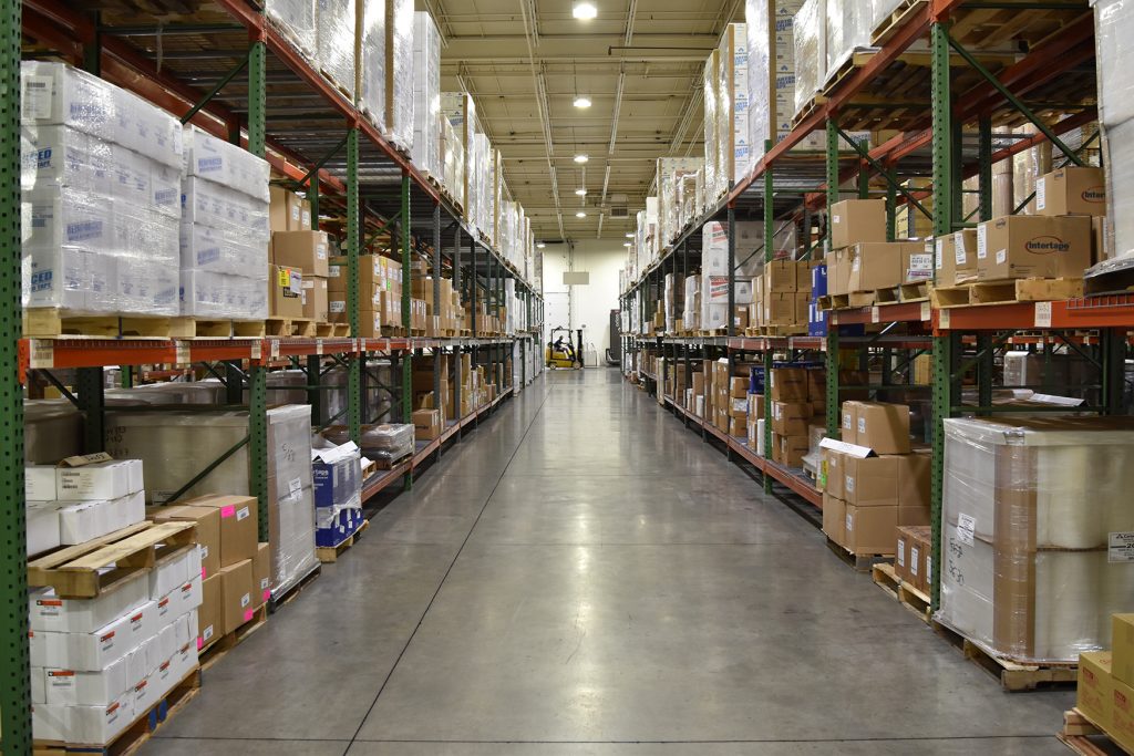 full warehouse with shelving on both sides and yellow forklift at end of center aisle 