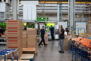 warehouse with workers, corrugated boxes stacked, and automated packaging line in back